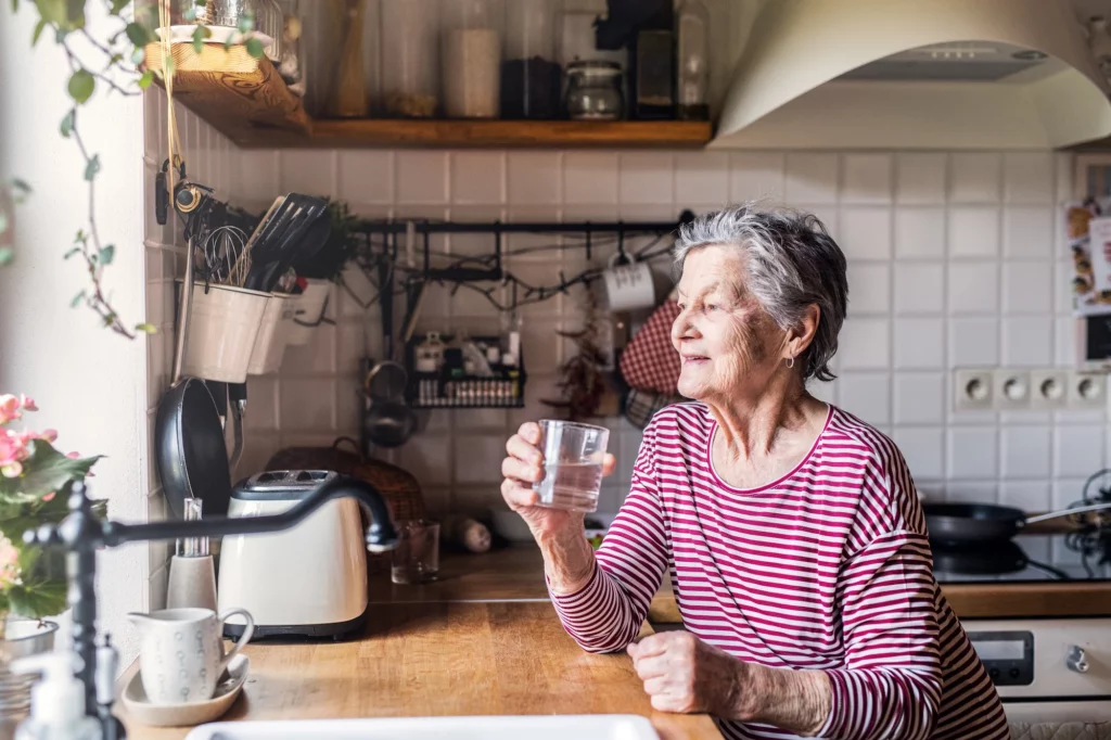 an elderly woman standing in the kitchen holding 2022 02 02 03 48 47 utc
